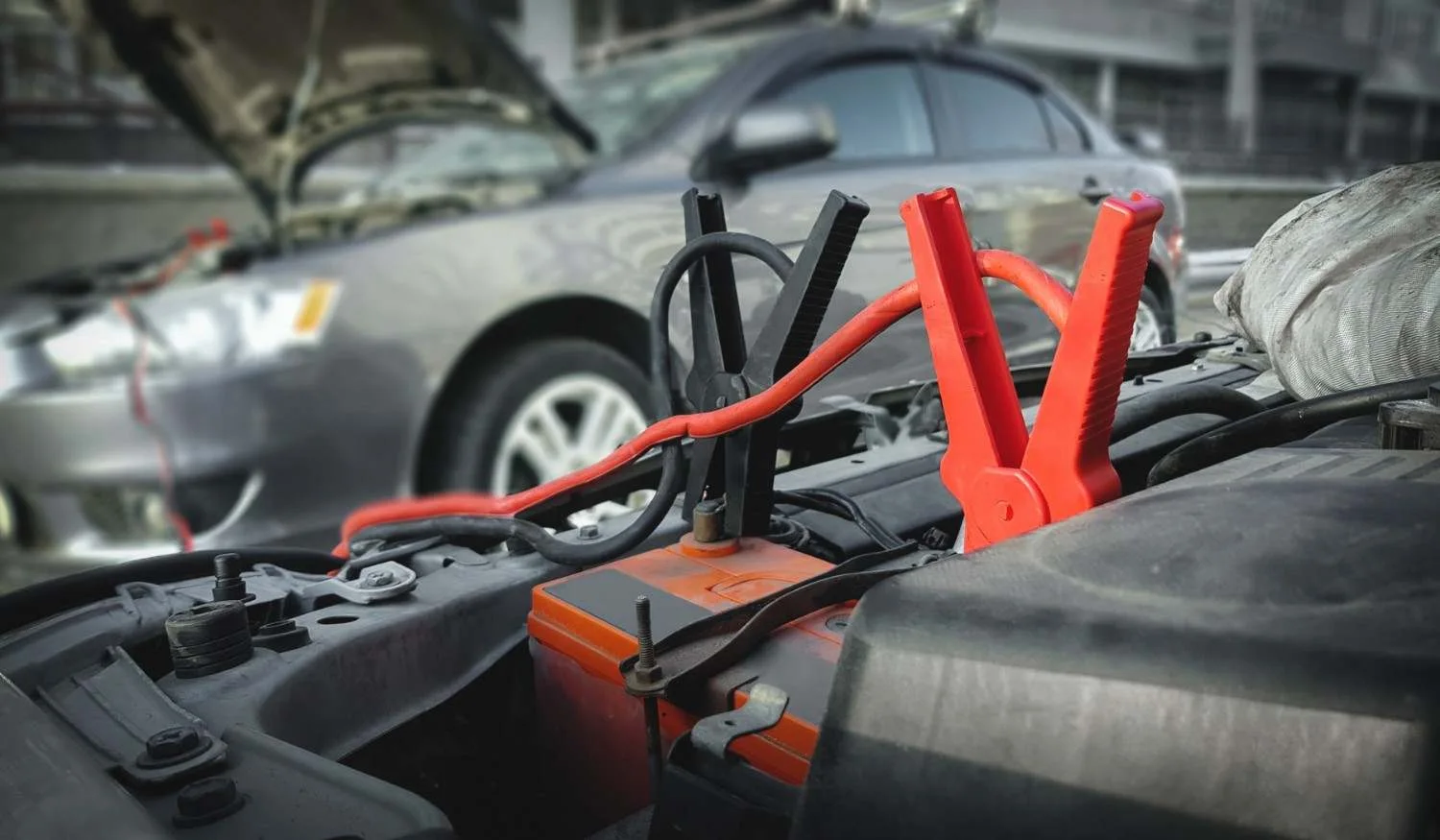 Red and black jumper cables connected to a car battery for a safe jump-start.