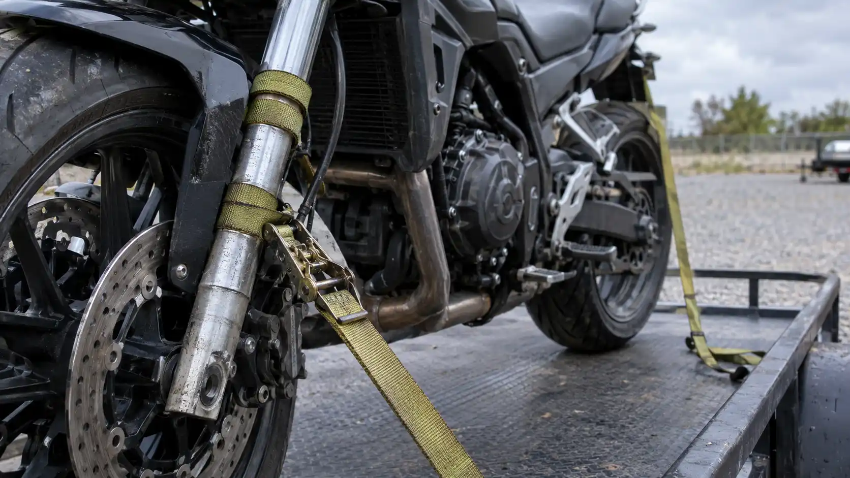 A close-up of a tie-down strap strapped directly to a motorcycle fork leg, illustrating mistakes that damage bikes during towing.