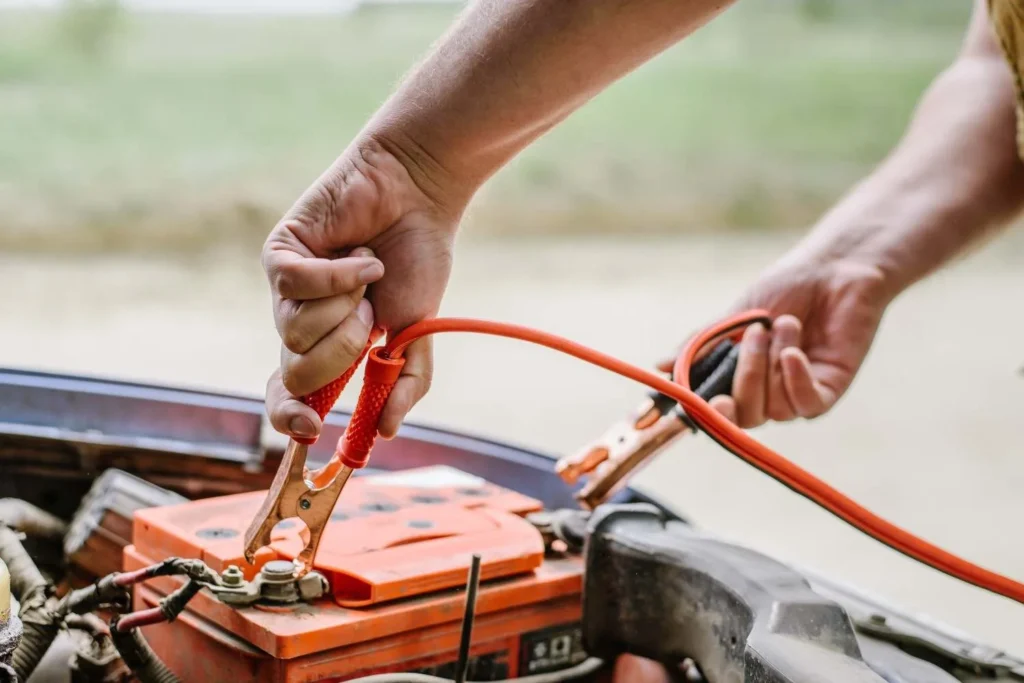 Person connecting jumper cables to a dead car battery under the hood.