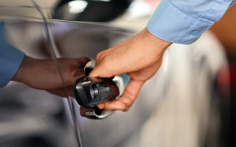 Close-up of a person's hand pulling a dark car door handle, illustrating how much should it cost to unlock a locked car.