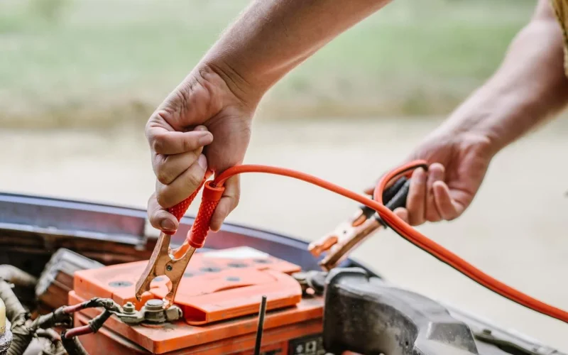 Person connecting jumper cables to a dead car battery under the hood.